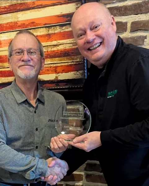 Keith Peterson holding the glass Micron award and shaking hands with the Micron representative who presented it